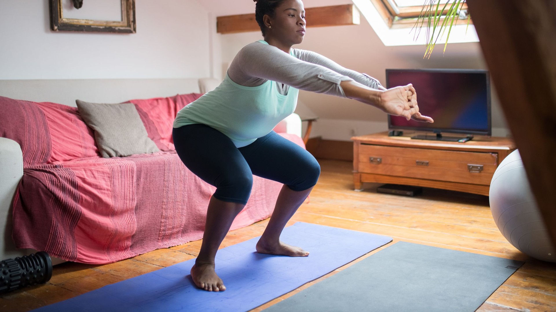 Woman doing a bodyweight squat on a yoga mat in her living room
